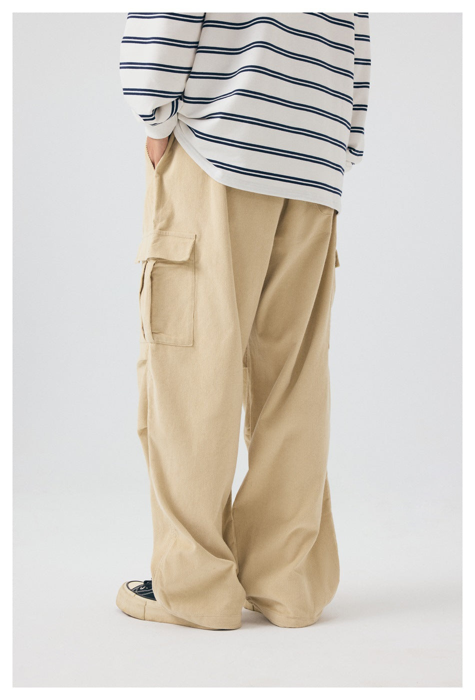 Rear view of a model wearing loose beige cargo pants with a large side flap pocket.