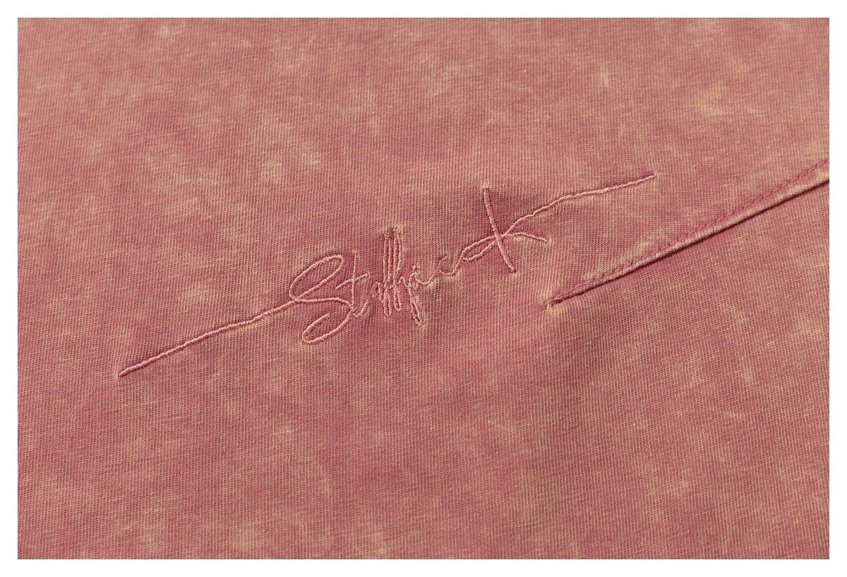 Close-up of cursive embroidery on the mottled pink fabric of a T-shirt.