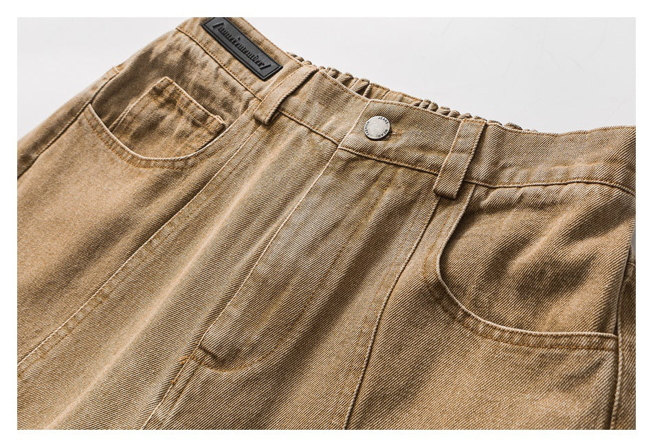 Close-up of the waistband, button, belt loops, and front pockets on tan washed jeans.