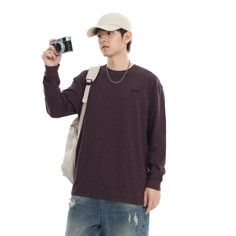 Model wearing a dark plum long-sleeve crewneck shirt with a beige cap, holding a camera against a white background.