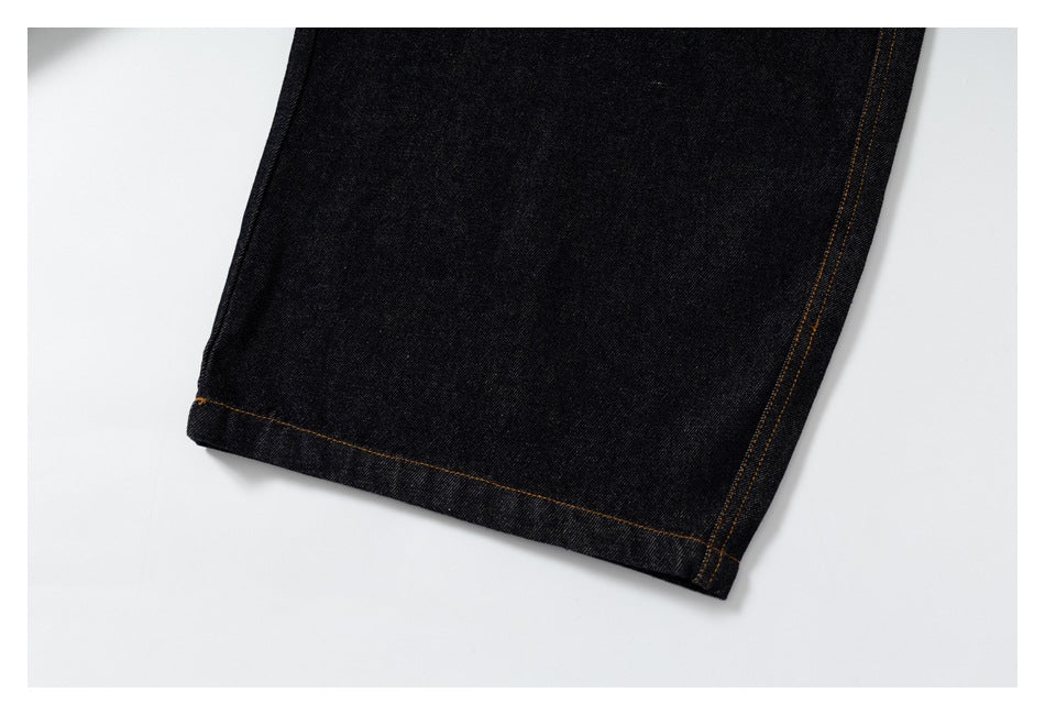 Close-up of a black denim pant leg hem with orange-brown stitching.