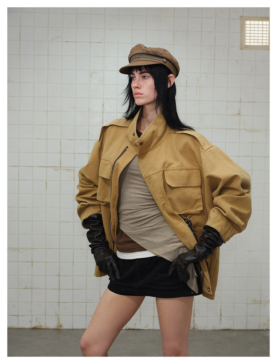 Model wearing an open tan utility jacket with flap pockets, layered tops, black gloves, and a black skirt.