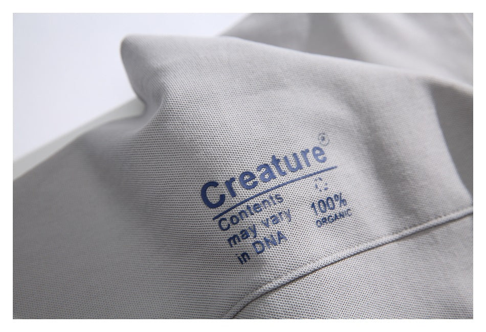 Close-up of light gray textured fabric with blue text reading “Creature Contents may vary in DNA, 100% organic.”