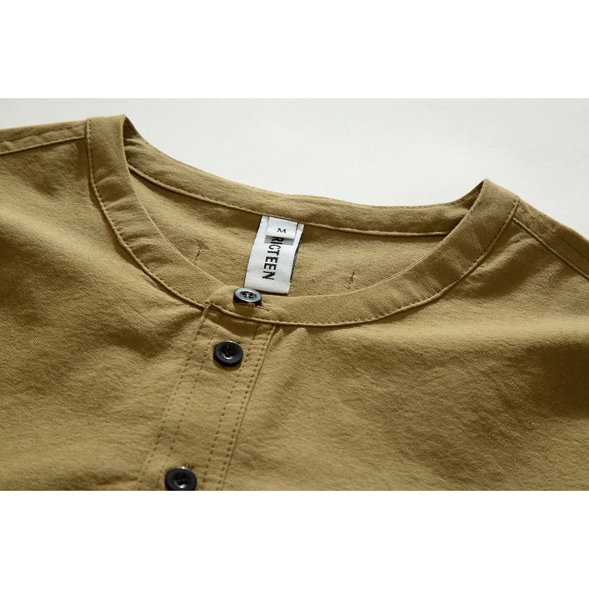 Close-up of a tan shirt's round neckline, three-button placket, and sewn-in neck label.
