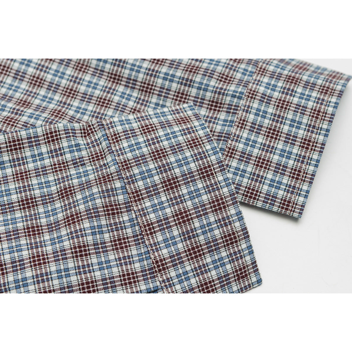 Close-up of blue, burgundy, and white plaid fabric with a stitched seam and cuff edge.