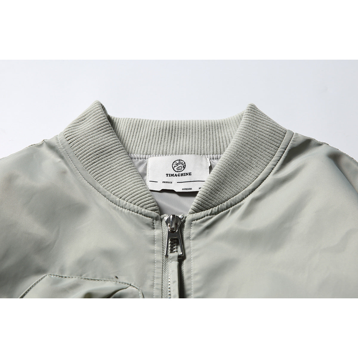 Close-up of a pale gray bomber jacket collar, front zipper, and sewn-in neck label.