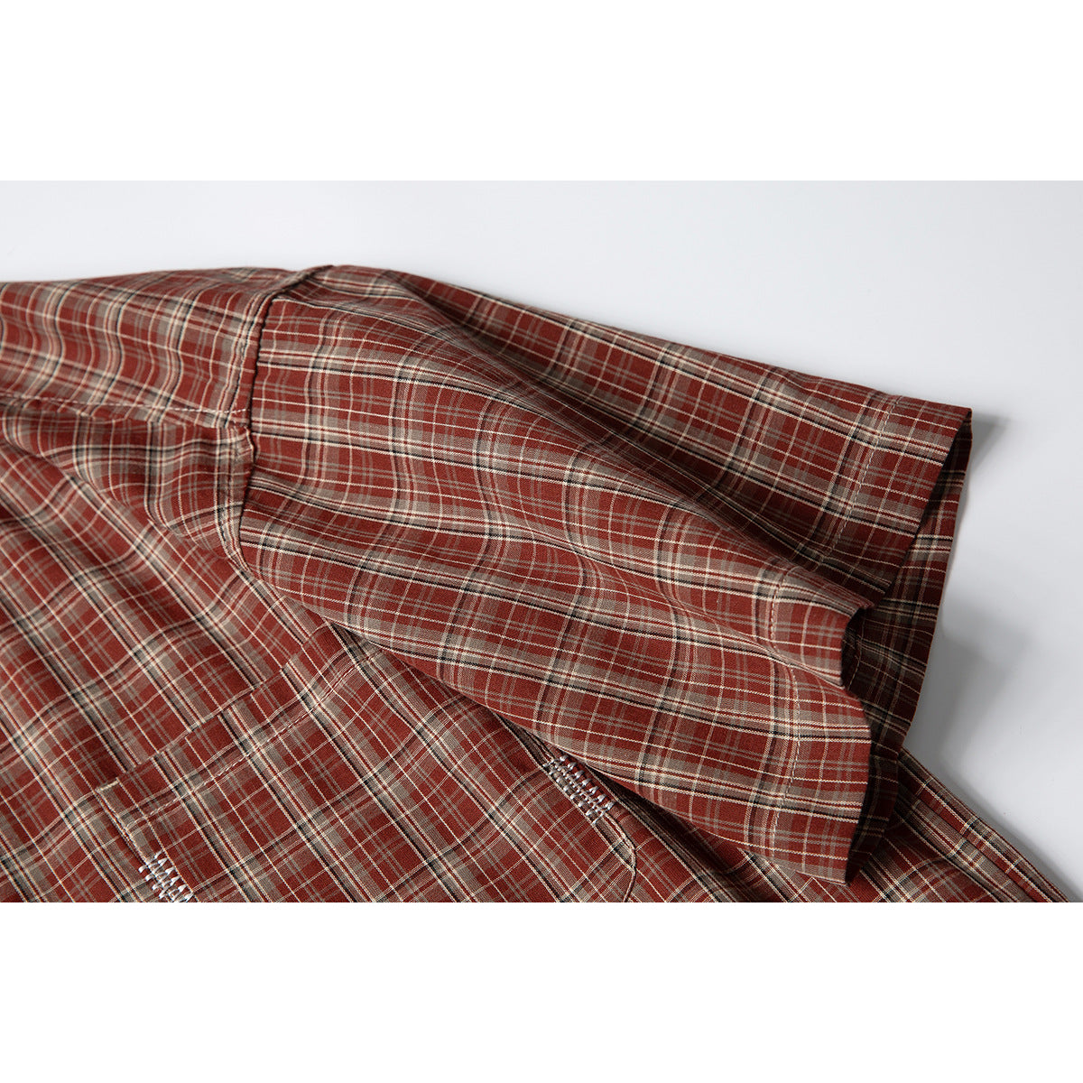Close-up of the rust-red plaid shirt's short sleeve, cuff, and stitched seams.