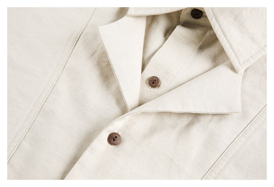 Close-up of an ivory shirt's open collar, brown buttons, and stitched seams.
