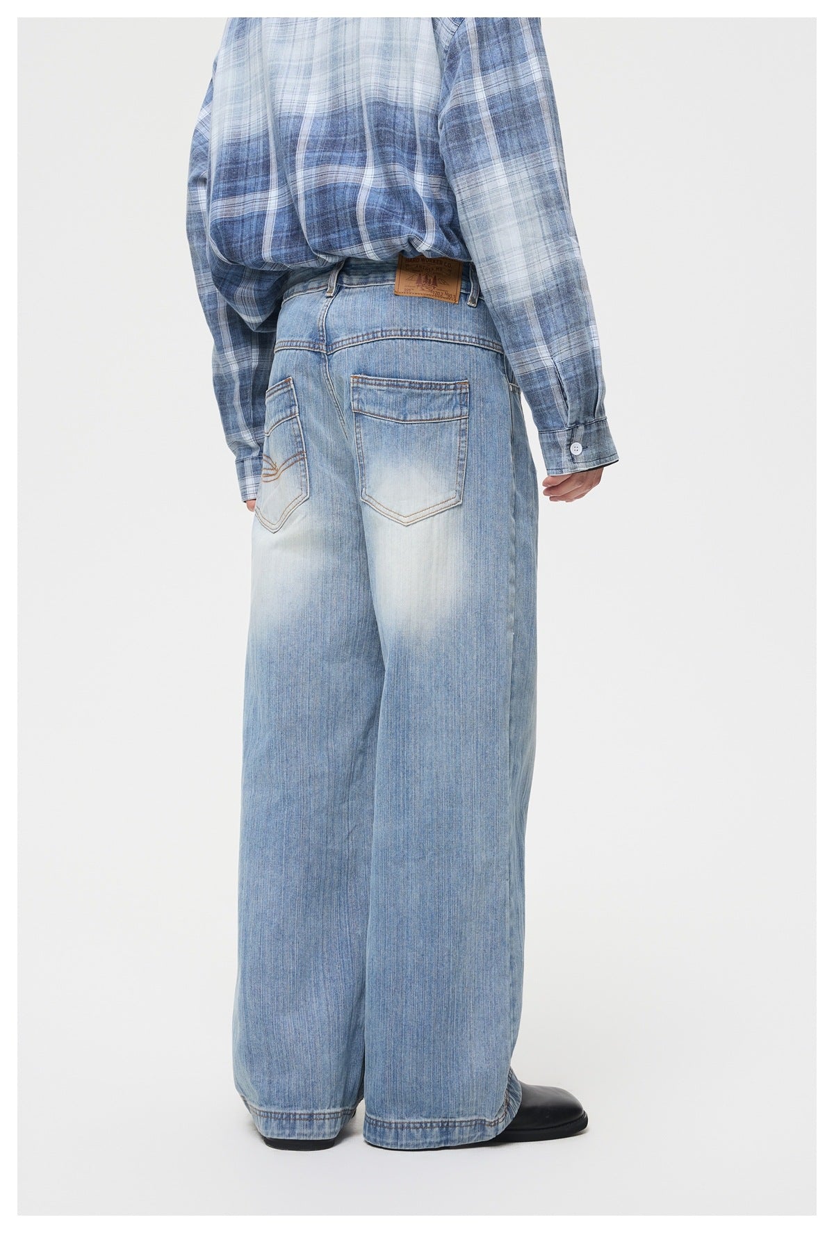 Cropped back view of a person wearing light blue faded, wide-leg jeans with two back pockets and a blue plaid shirt.