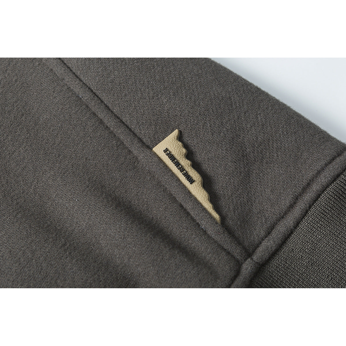 Close-up of a beige branded tab set into a seam on charcoal sweatshirt fabric.