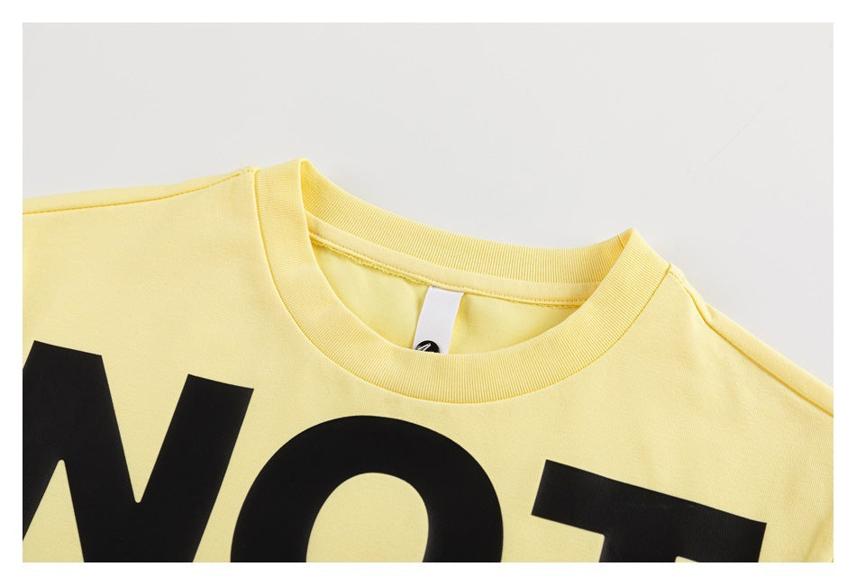 Close-up of the pale yellow T-shirt crew neckline, shoulder seam, and part of its black front lettering.