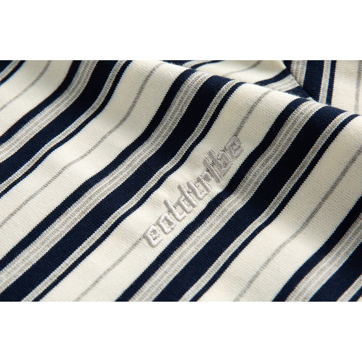 Close-up of pale embroidered lettering on cream fabric with navy and gray stripes.