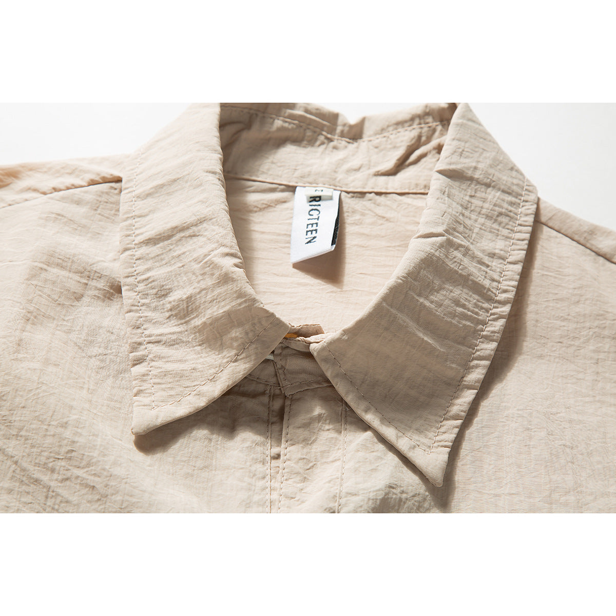 Close-up of a beige shirt’s wide pointed collar and inner neck label.