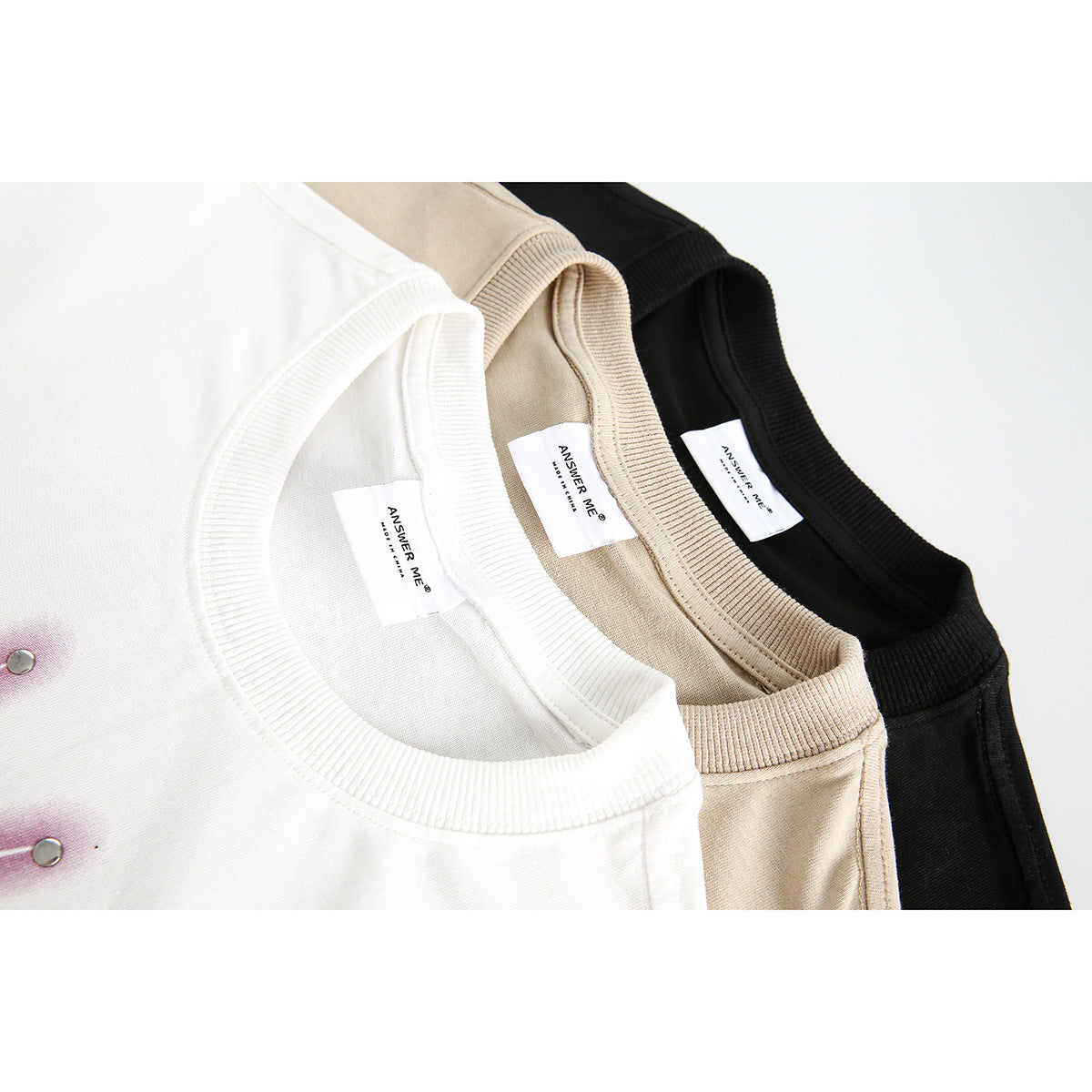 Close-up of white, beige, and black T-shirt collars with ribbed neckbands and inner brand labels.