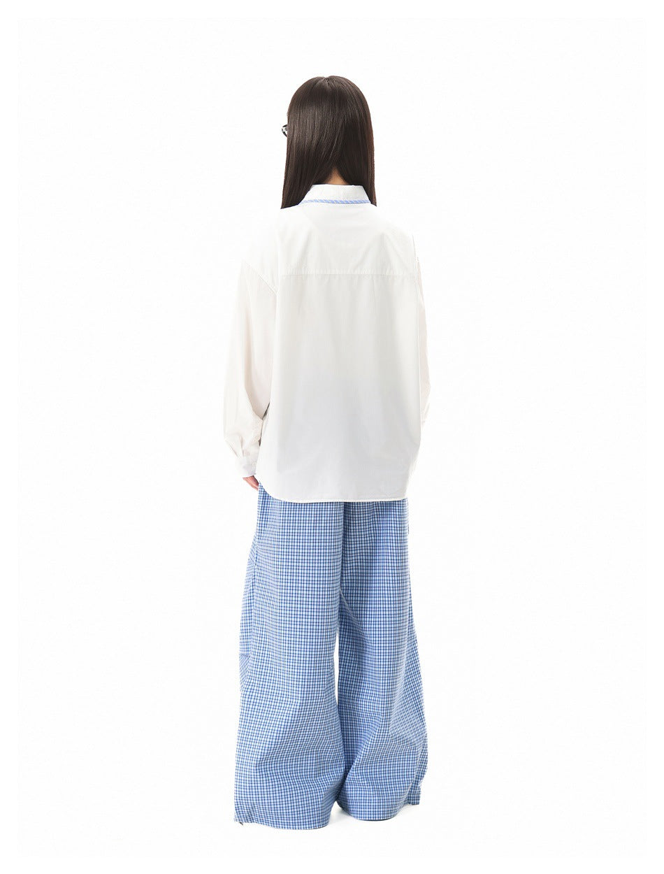 Back view of a model wearing a white shirt with blue striped collar and blue checked wide-leg trousers.