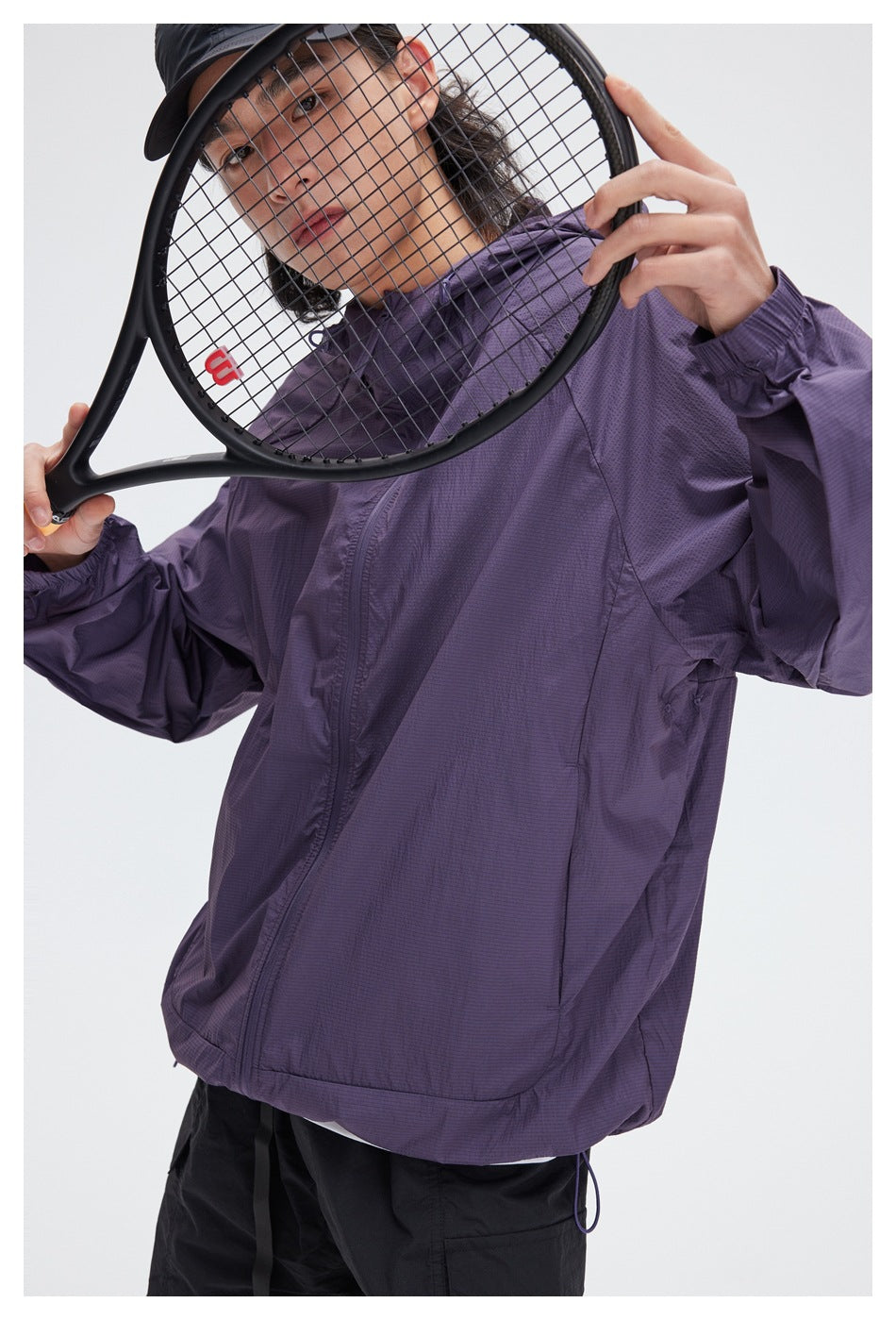 Close view of a purple hooded jacket worn by a person, with a tennis racket in the foreground.