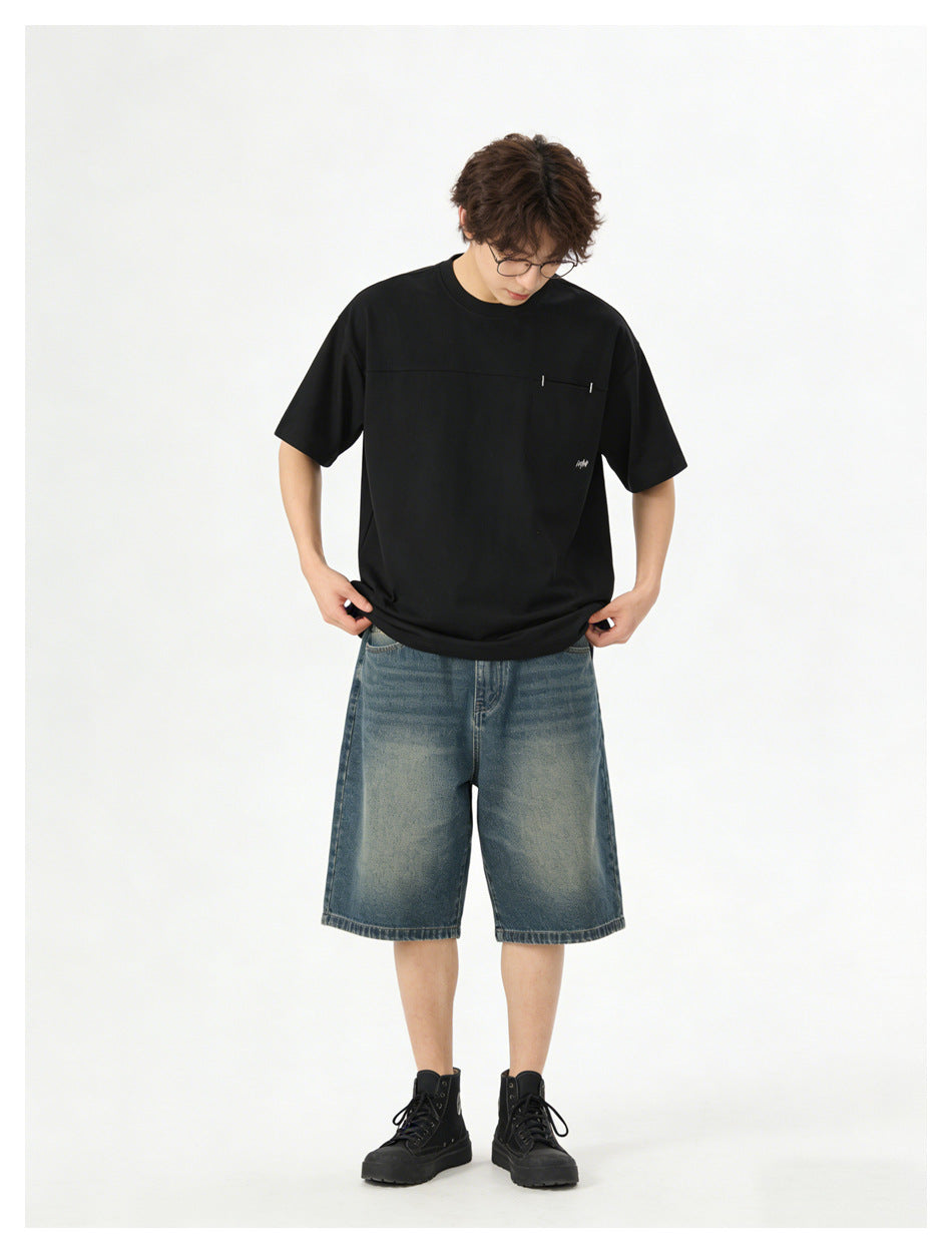 Model wearing a black short-sleeve T-shirt with a horizontal chest seam and blue denim shorts, front view.