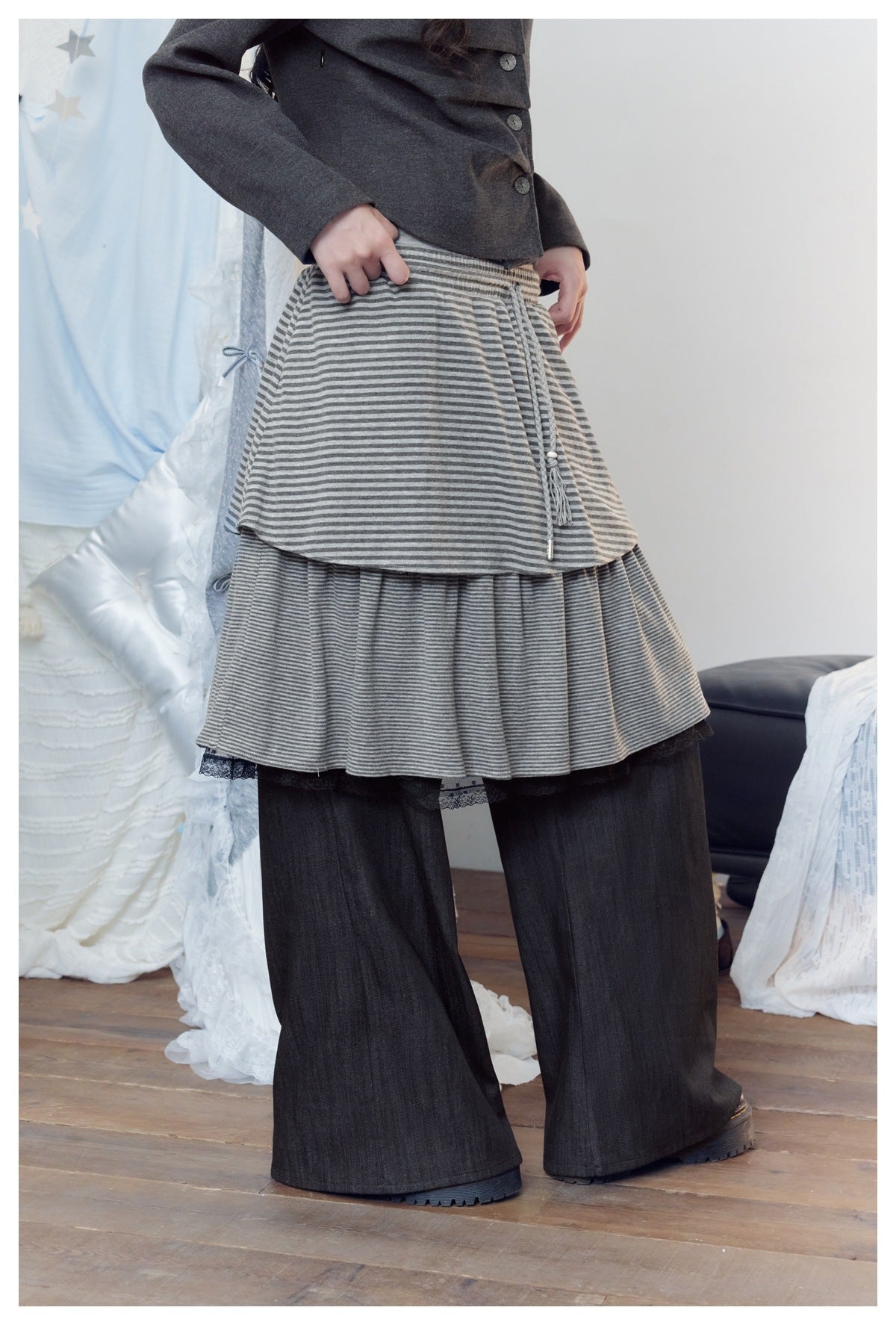Model wearing a gray striped, layered skirt with drawstring over wide black pants, shown from the front.