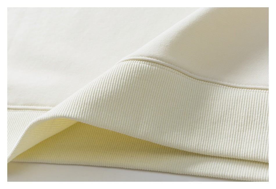 Close-up of an ivory garment's ribbed knit edge and seam, with the fabric folded back.