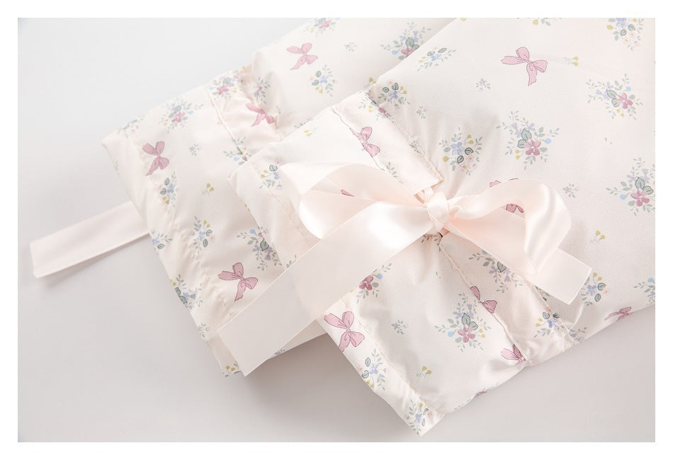 Close-up of a pale ivory floral-and-bow printed garment tied with a wide pale pink satin ribbon.