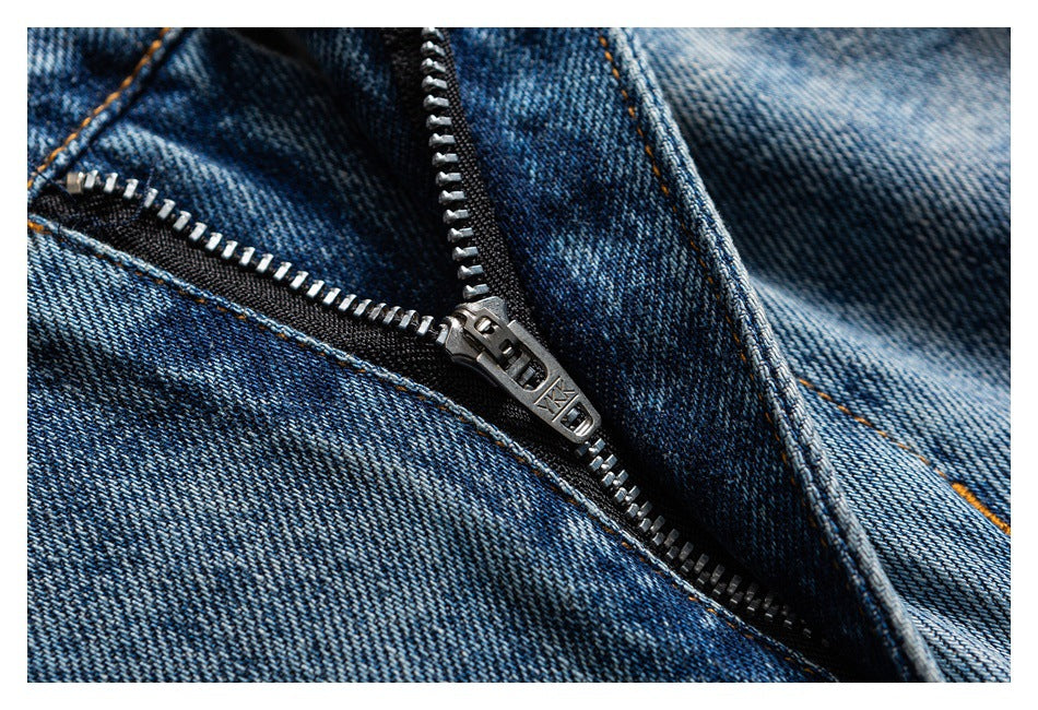 Close-up of a metal zipper on dark blue denim with orange contrast stitching and textured fabric.