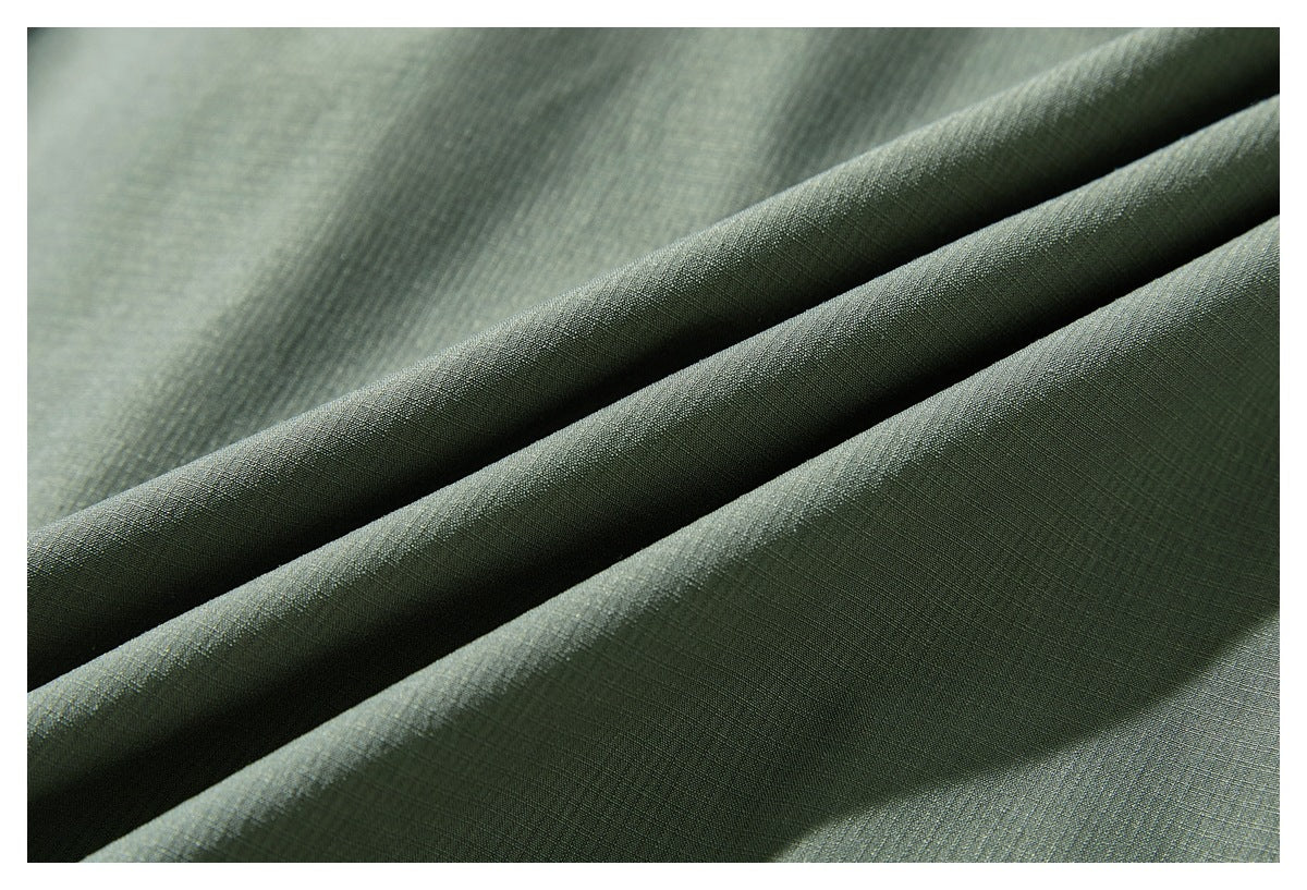 Close-up of sage-green jacket fabric draped in folds, showing its fine surface texture.