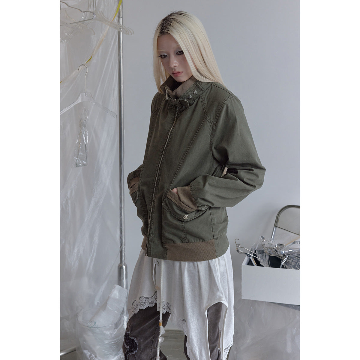 Model wearing an olive zip-front jacket with a high buckled collar, flap pockets and taupe ribbed trim.