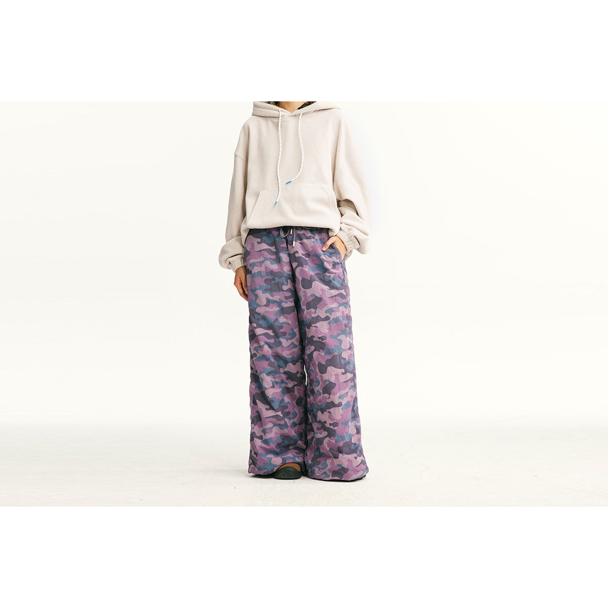 Cropped model wearing a light beige hoodie and loose purple camouflage pants.