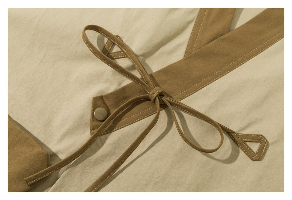 Close-up of a beige garment with a brown tie belt knotted through a stitched fabric loop and a snap tab.