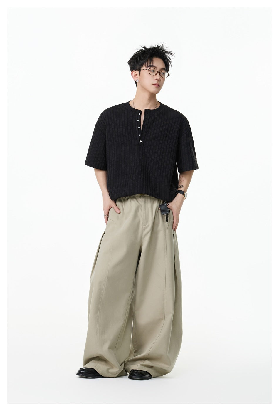 Model wearing a black ribbed short-sleeve henley with beige wide-leg trousers.