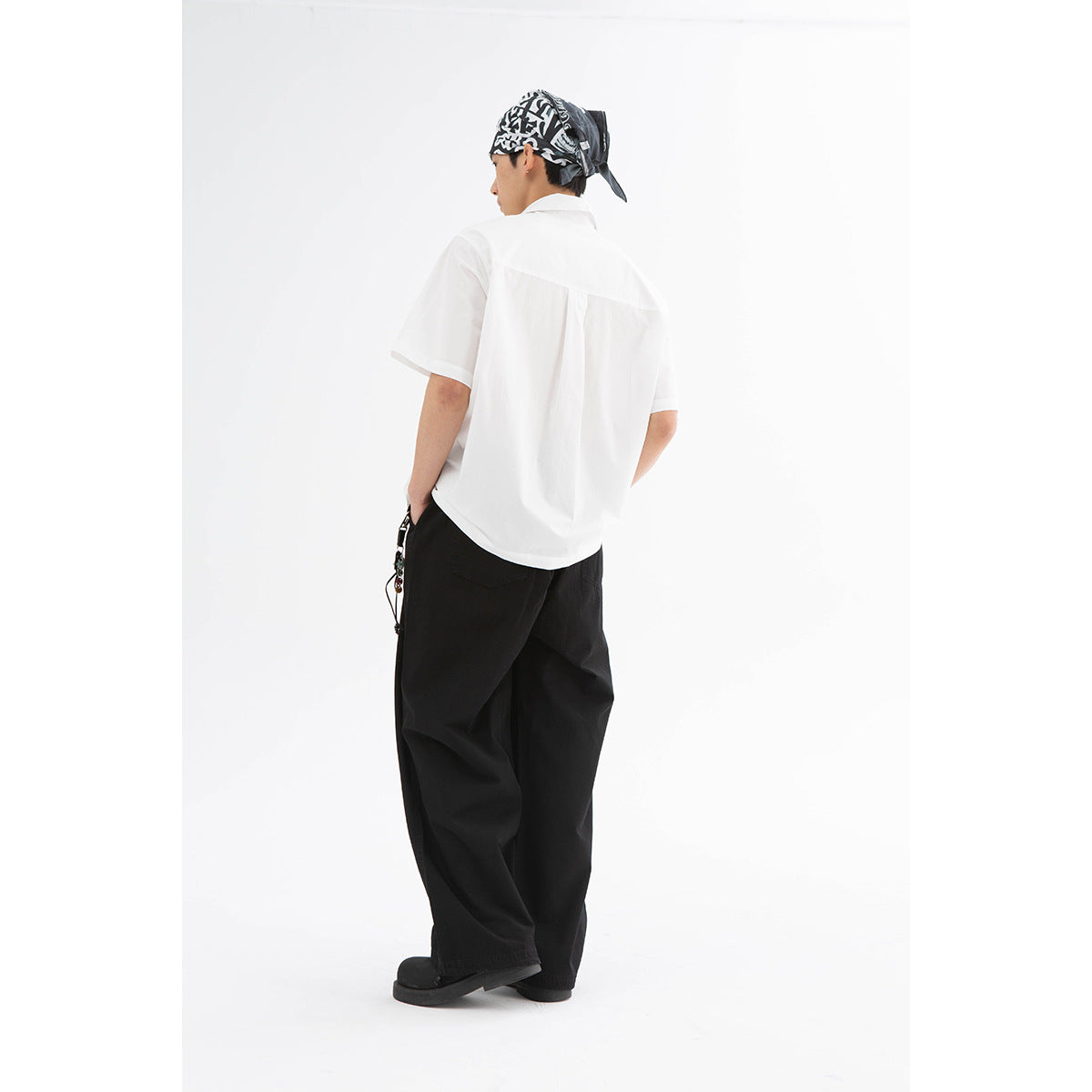 Rear view of a model wearing a white short-sleeve shirt and loose black trousers.