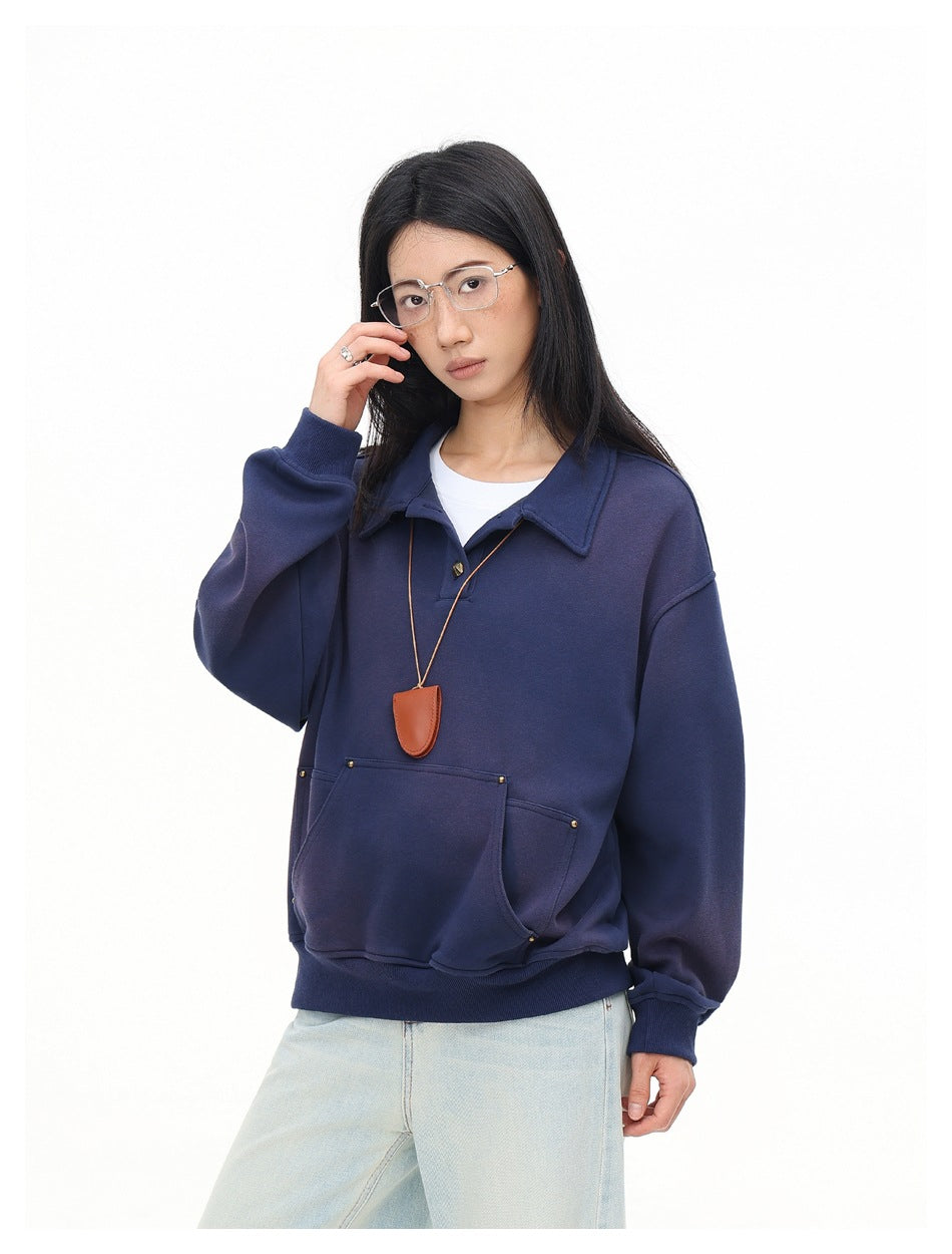 Model wearing an oversized navy collared sweatshirt with gold buttons, a studded kangaroo pocket and ribbed cuffs.