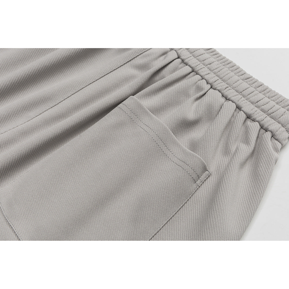 Close-up of a pocket and gathered elastic waistband on light gray shorts.
