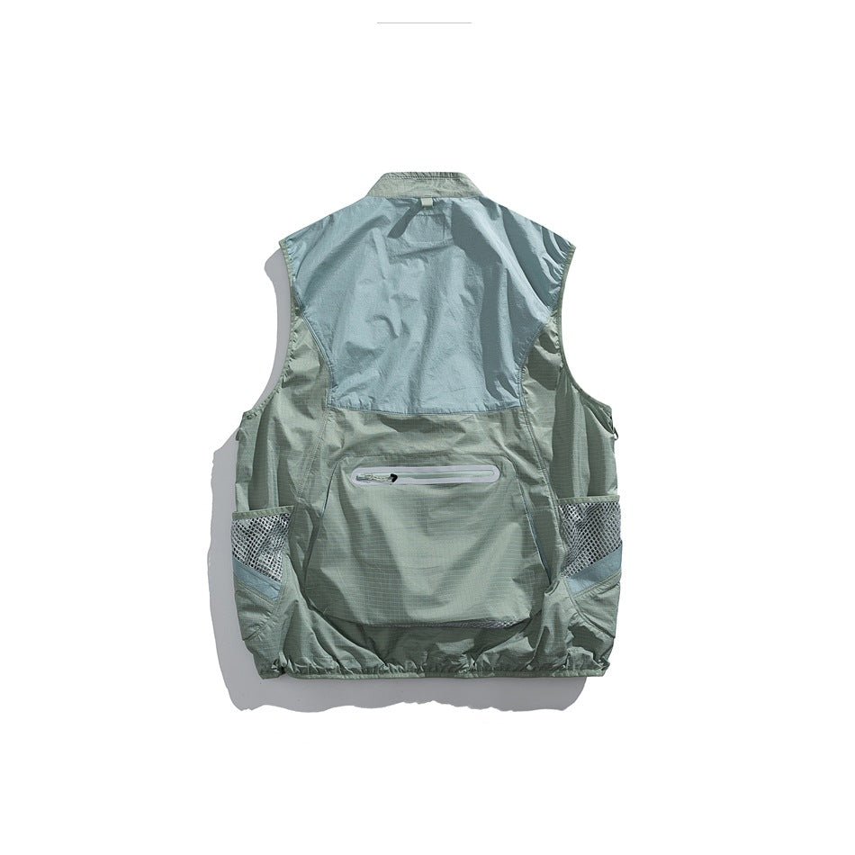 Back view of a sage green utility vest with a pale blue-gray back panel, zip pocket, and mesh side pockets.