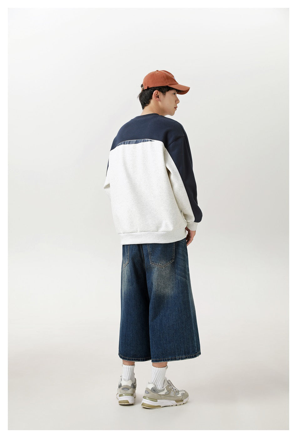 A model shows the back of a cream-and-navy color-block sweatshirt with dark wide-leg denim bottoms.