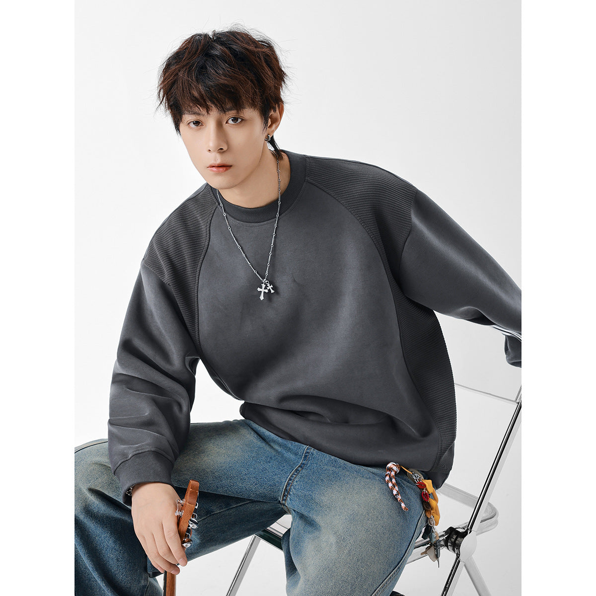 Seated model wearing a charcoal gray crewneck sweatshirt with textured shoulder and side panels.