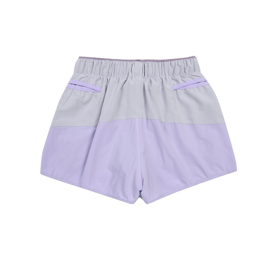 Back view of color-block athletic shorts in light gray and lavender with an elastic waistband and angled pocket openings.