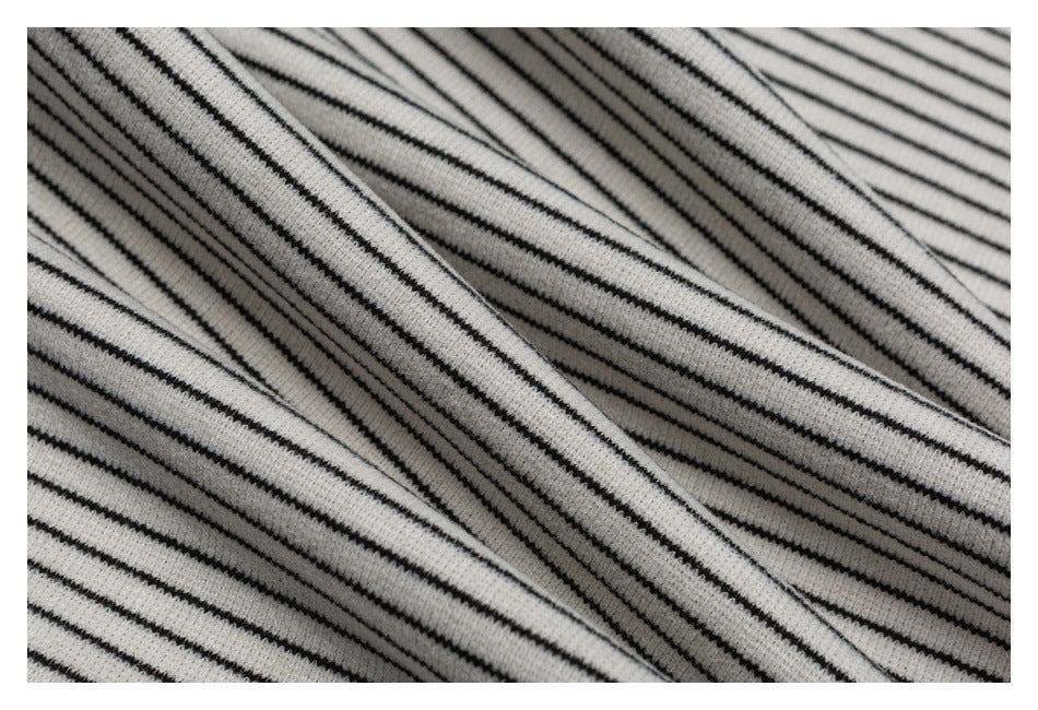 Macro view of off-white knit fabric with narrow black stripes draped in diagonal folds.