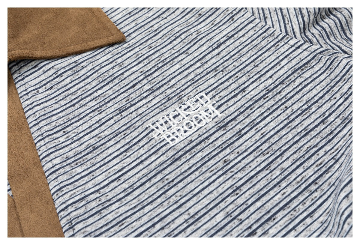 Close-up of white embroidered lettering on the gray and navy striped fabric beside tan trim.