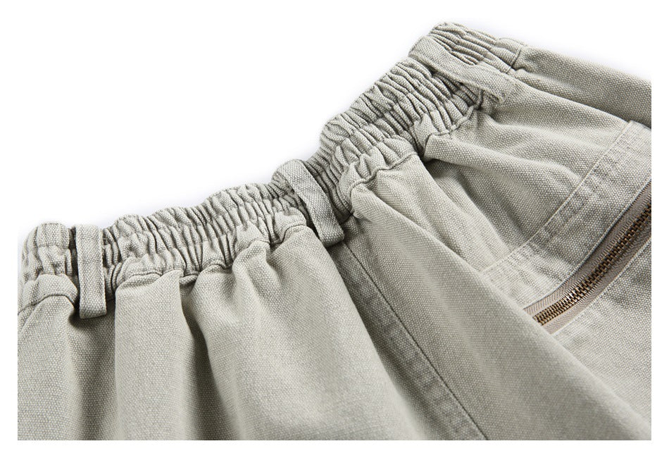 Close-up of light gray-beige bottoms showing an elasticated waistband, belt loops, and a metal zipper.