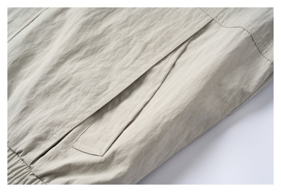 Close-up of a light beige jacket showing a slanted welt pocket and stitched seams.