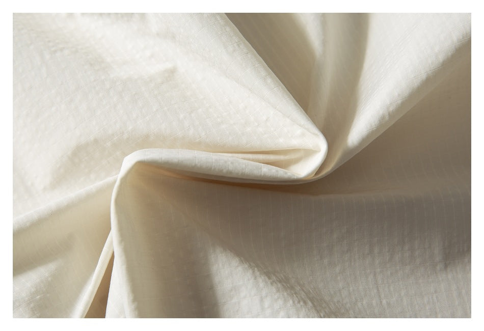 Close-up of softly draped ivory shirt fabric showing its subtle woven texture.