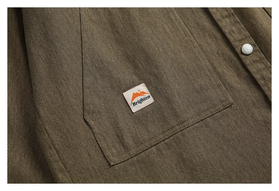Close-up of the jacket's small sewn-on pocket patch against brown-olive twill fabric.