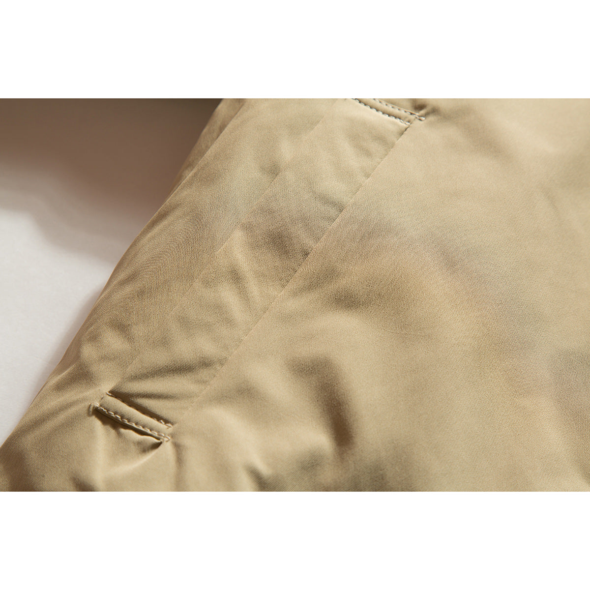 Close-up of tan jacket fabric and a small welt pocket.