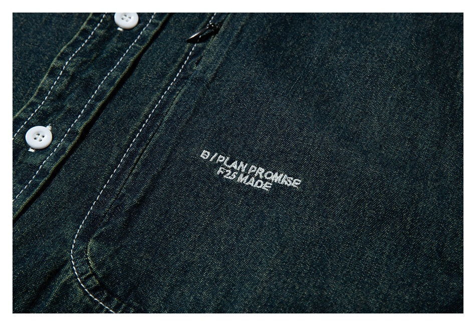 Close-up of white embroidered lettering on the chest of a dark blue-green shirt.