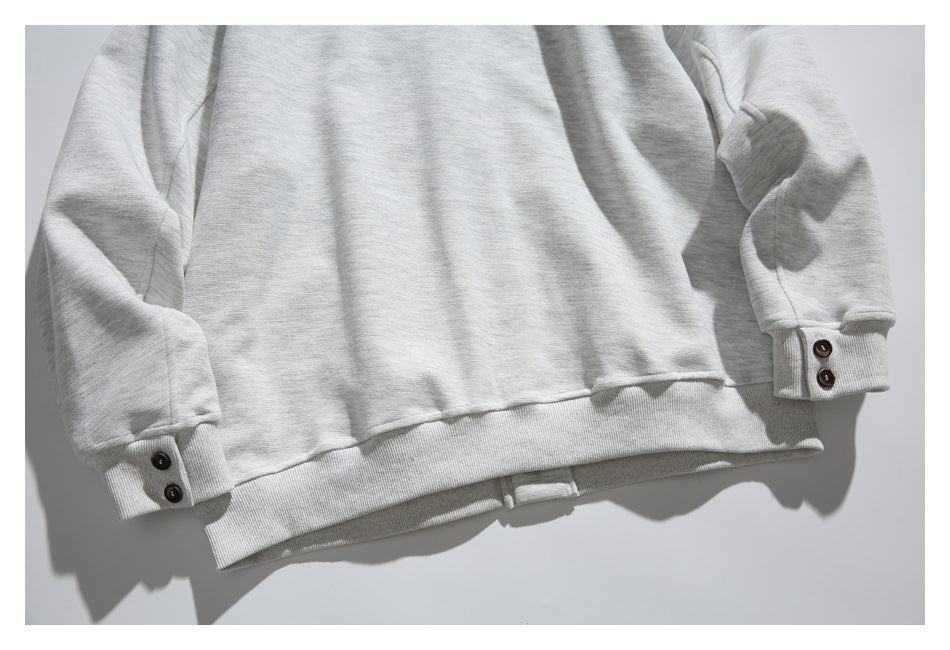Lower portion of a light gray sweatshirt laid flat, showing long sleeves, buttoned cuffs, and a ribbed hem.