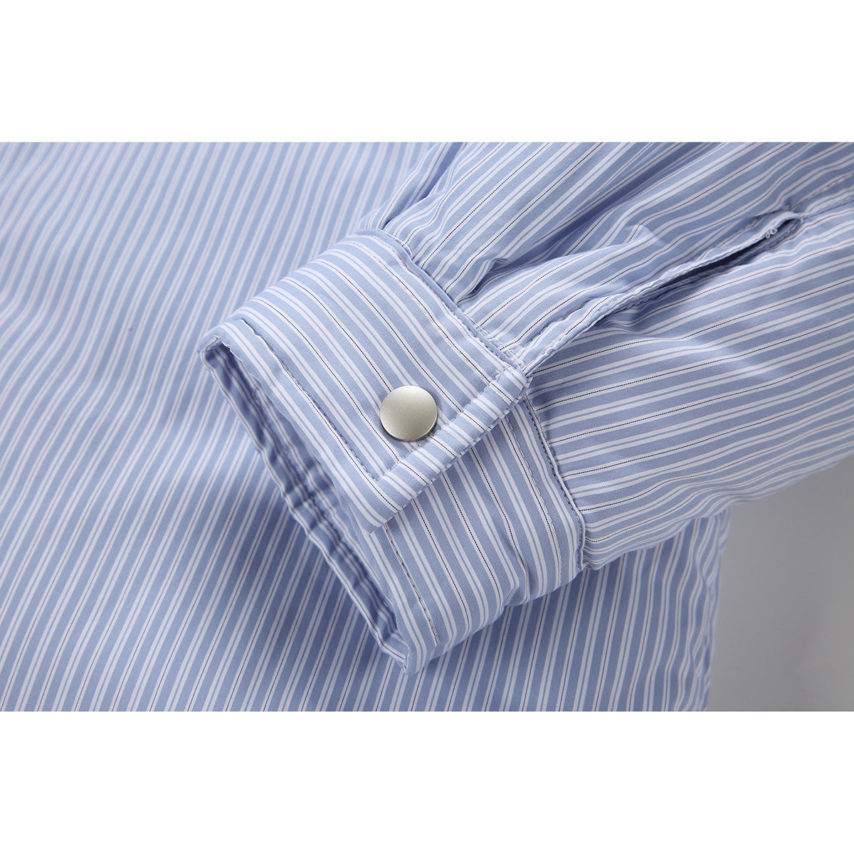 Close-up of a wide cuff with a silver snap button on a light blue and white striped sleeve.