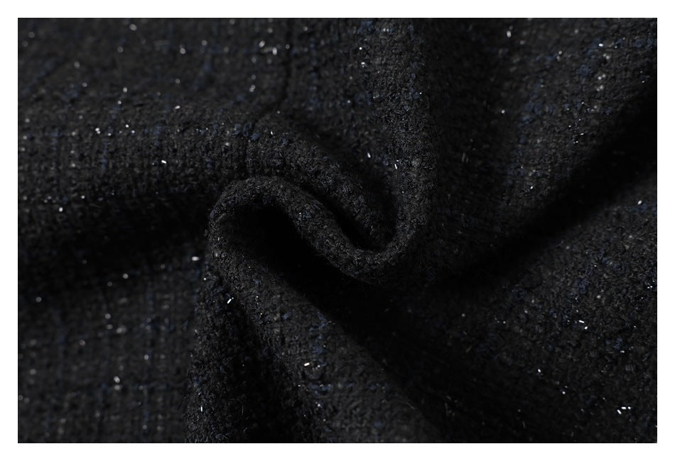 Close-up of black textured fabric gathered into a soft fold, with scattered reflective flecks.