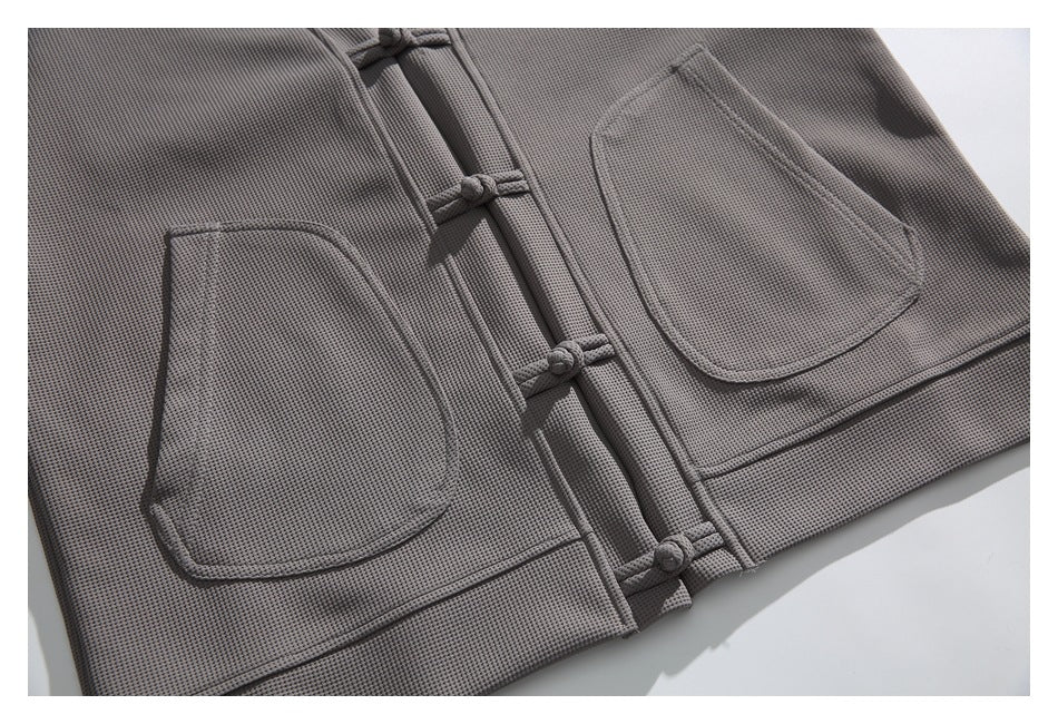 Close-up of the gray jacket front with two patch pockets and several knotted frog closures.