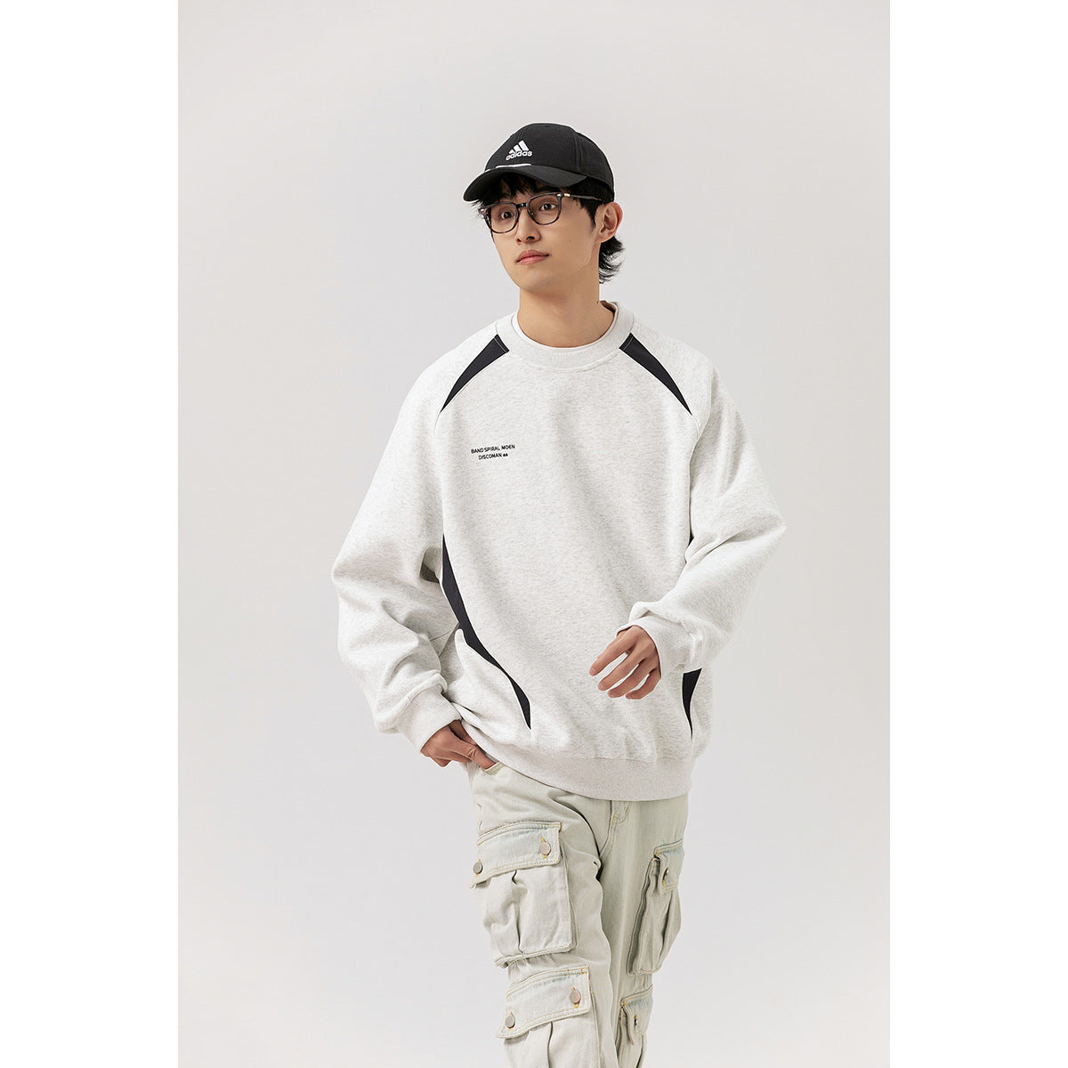 Model wearing a light gray crewneck sweatshirt with black shoulder and side panels, shown from the front.